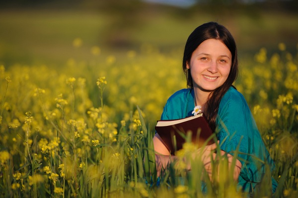 babaeng nakaupo sa batawan ng bulaklak habang hawak ang Bibliya