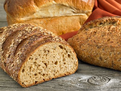 miches de pain complet aux céréales, et pain brioché, sur table en bois, avec nappe (serviette) tissu rouge orangé.