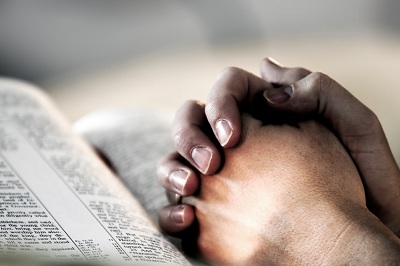gefaltene Hände ruhen auf einer geöffneten Bibel