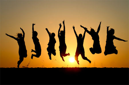 silhouettes de personnes sautant de joie sur le sable au soleil couchant