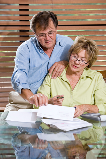 Un couple de personnes âgées / mûres regardant / examinant leurs factures pour faire les comptes.