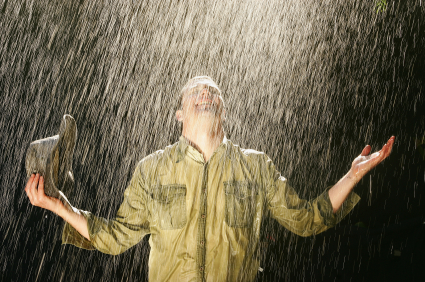 Agriculteur souriant debout sous la pluie, son chapeau à la main, son visage offert à l’eau, les bras écartés en signe de reconnaissance; image, métaphore de la pluie de l’arrière saison de l’Esprit Saint.