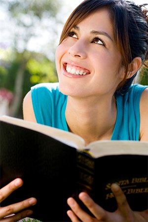 Jeune fille souriante, les yeux levés vers le ciel, tenant une Bible dans ses mains, dans un parc naturel.