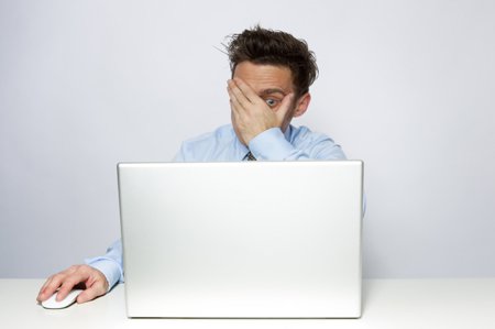 man peeking through hands at a computer screen