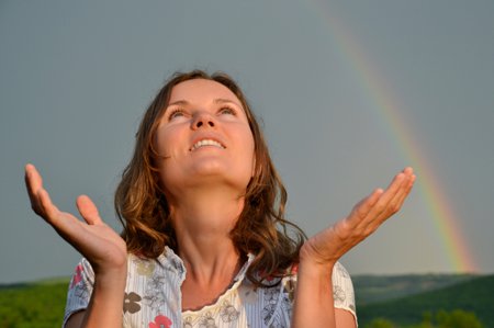 une femme au visage radieux, heureuse et souriante, libérée, regardant avec reconnaissance et joie vers le Ciel, avec un arc-en-ciel et la nature à l'arrière-plan, les bras levés écartés en prière, les mains tournées vers le haut; la victoire sur la masturbation et la pornographie, comment surmonter, vaincre