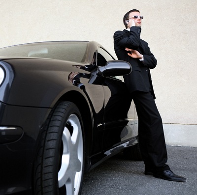 man leaning against expensive car while talking on a cell phone