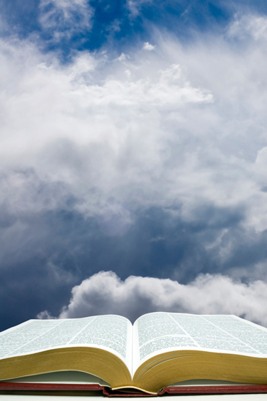 Open Bible in front of blue sky with clouds