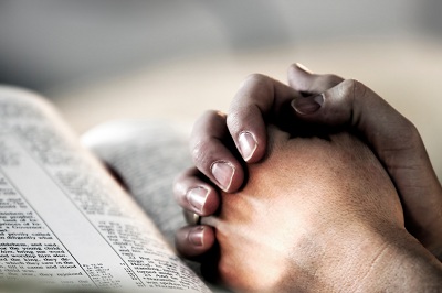 folded hands resting on open Bible