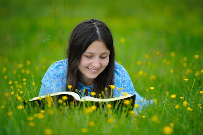 young similing girl reading Bible outdoors