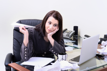 woman sitting at a messy desk, holding a paper airplane (wasting time)