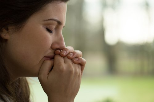 femme en deuil, pleurant, les mains jointes au visage, comme en prière, sur fond vert naturel