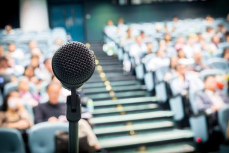 microphone dynamique placé devant une grande foule, auditoire public en estrade, gradins étagés, sièges et rangs, avec escalier central; église, salle de conférence, auditorium, amphithéatre, ou salle de cours universitaire