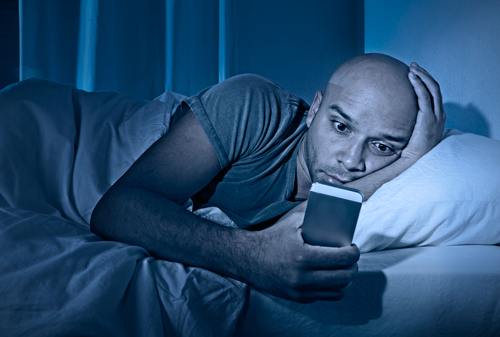 un homme couché dans un lit fixant des yeux son smartphone