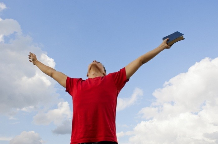Homme avec les bras élevés au ciel et une Bible dans sa main (portant un t-shirt rouge)