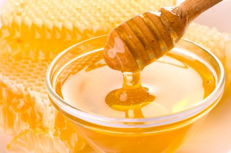 miel coulant d’une cuillère à miel (baguette de bois) dans un bol (coupelle) et rayon de miel, en structure nid d'abeille, cire gaufrée