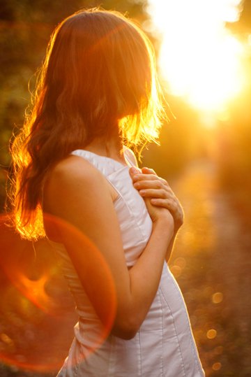 jeune femme en robe blanche aux longs cheveux blond chatain clair aux reflets dorés, regardant le soleil levant ou couchant sur le chemin dans la nature