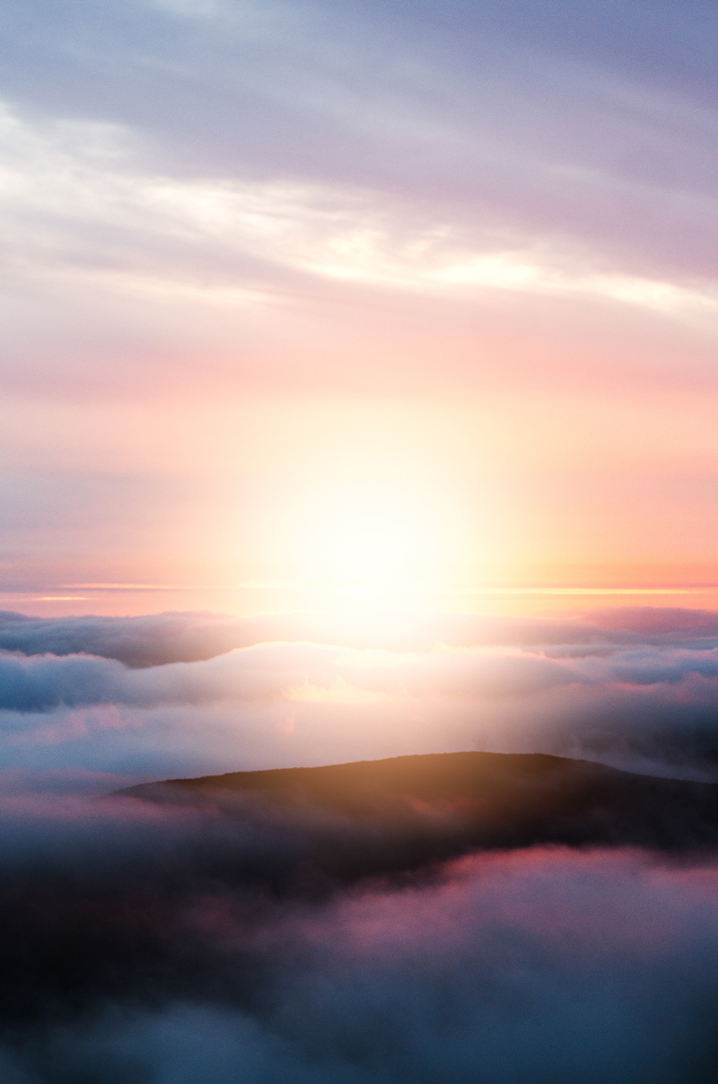 représentation, notion de la glorification, idée de la Gloire céleste; image photographique d’un matin au lever du soleil, d’un point de vue supérieur, au-dessus des nuages et des sommets des montagnes, avec le dégradé des couleurs du blanc au jaune, orangé, rosé, avec une luminosité centrale