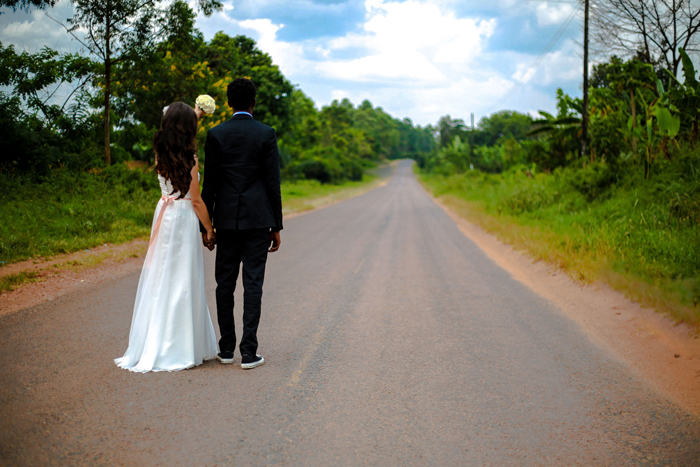 couple se tenant la main, habillés d’un costume noir et d’une robe blanche, regardant dans la même direction sur une route