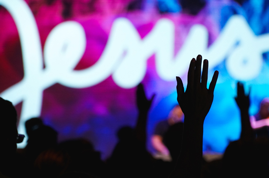 chrétiens mondains; assemblée de louange évangélique, levant les mains lors d’un concert de musique mondaine contemporaine chrétienne, avec un néon géant blanc au nom de Jésus.