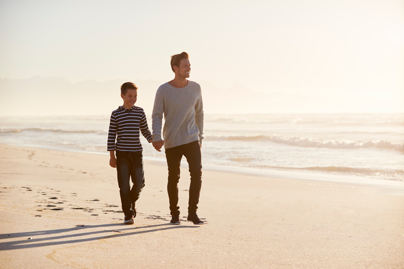 père et fils souriants, marchant main dans la main sur une plage de sable blanc au bord de la mer