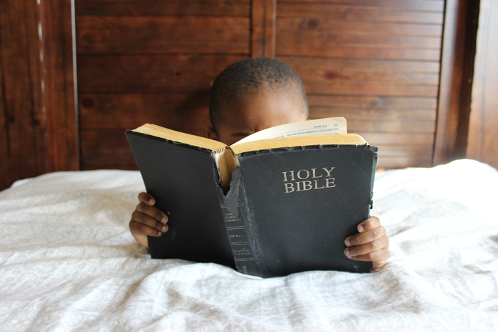 enfant lisant une grande Bible noire au lit