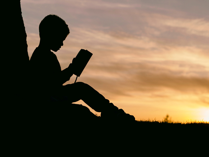 enfant dans l’ombre, adossé à un arbre, lisant la bible en soirée