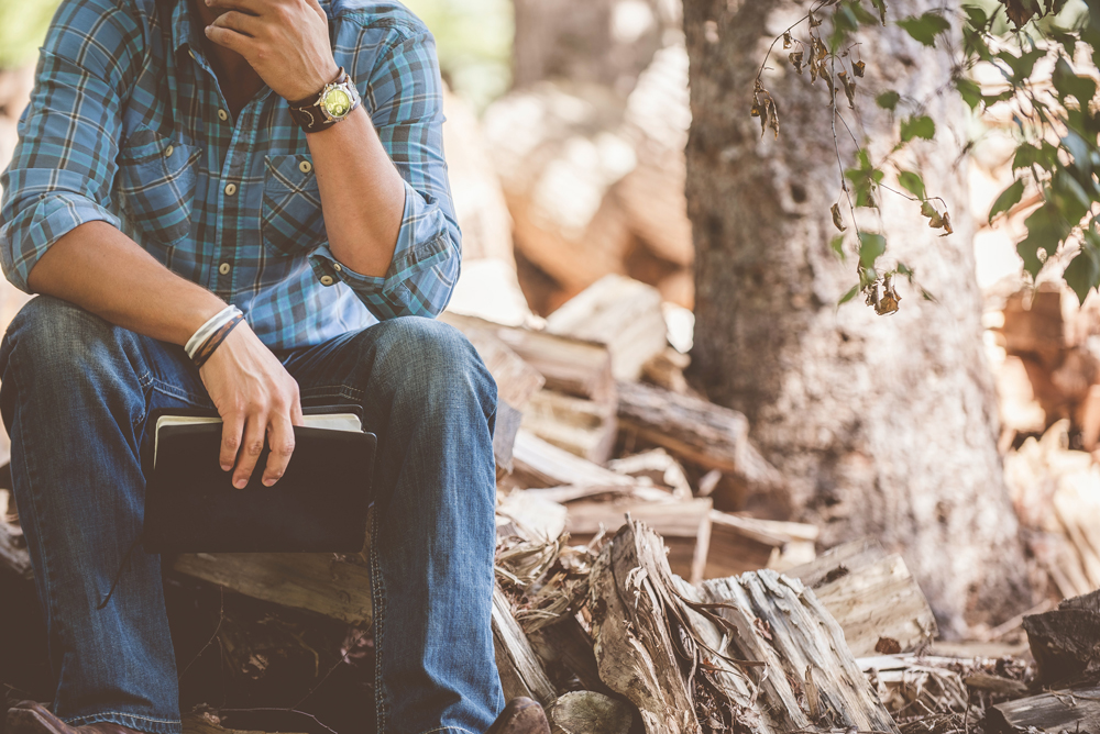 man sitting in the woods, holding a Bible